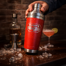 Load image into Gallery viewer, Hand holding a red Rudy’s Bar &amp; Grill YETI cocktail shaker surrounded by ice, jigger, liquor bottle, and cocktail on a bar.