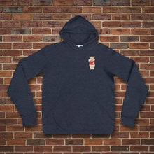 Load image into Gallery viewer, Navy blue hoodie featuring a small Baron Von Swine pig mascot graphic on the chest, displayed flat against a reddish-brown textured brick wall background. The hoodie is centered and well-lit for a realistic