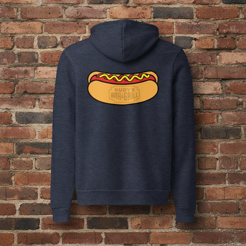 Navy blue hoodie featuring a large Rudy’s Bar & Grill hot dog logo on the back, displayed against a reddish-brown textured brick wall background. The hoodie is centered and well-lit, creating a realistic product mockup for Rudy’s Bar & Grill merchandise