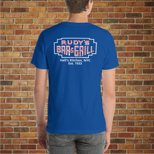 Load image into Gallery viewer, Model showing the back of a true royal blue Rudy’s Bar &amp; Grill t-shirt with a neon sign logo and “Hell’s Kitchen, NYC Est. 1933” text, standing against a brick wall backdrop.