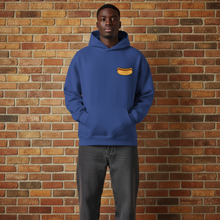 Load image into Gallery viewer, Front view of Rudy’s Bar &amp; Grill Hot Dog Neon Hoodie in cobalt blue, worn by a model, featuring the hot dog logo on the chest, displayed against a brick wall background.
