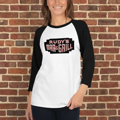 Person wearing a Rudy’s Bar & Grill black and white baseball shirt standing in front of a rustic brick wall background, smiling, with the Rudy’s Bar & Grill logo clearly visible on the shirt.