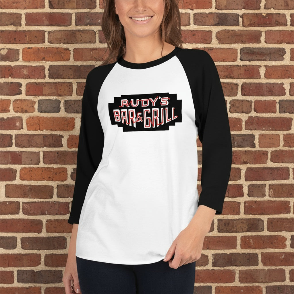 Person wearing a Rudy’s Bar & Grill black and white baseball shirt standing in front of a rustic brick wall background, smiling, with the Rudy’s Bar & Grill logo clearly visible on the shirt.
