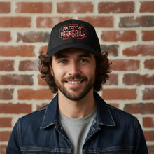 Load image into Gallery viewer, A smiling man wearing a black Rudy’s Bar &amp; Grill hat, standing in front of a brick wall