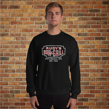 Load image into Gallery viewer, Man wearing black Rudy’s Bar &amp; Grill Hell’s Kitchen NYC neon sign sweatshirt in front of a brick wall