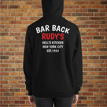 Load image into Gallery viewer, Model wearing Rudy’s Bar Back Hoodie in black, showing “BAR BACK RUDY’S HELL’S KITCHEN NEW YORK CITY EST. 1933” text on the back, brick wall background