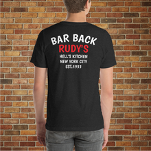 Load image into Gallery viewer, Back of Rudy’s Bar &amp; Grill Bar Back T-Shirt in black heather, worn by a male model, with “Bar Back Rudy’s Hell’s Kitchen New York City Est. 1933” printed, displayed against a brick wall background