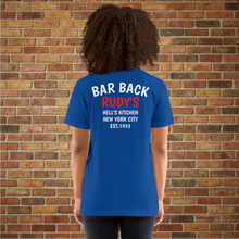 Load image into Gallery viewer, Back of Rudy’s Bar &amp; Grill Bar Back T-Shirt in royal blue, worn by a female model, with “Bar Back Rudy’s Hell’s Kitchen New York City Est. 1933” printed, displayed against a brick wall background