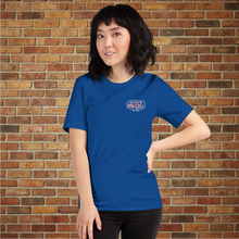 Load image into Gallery viewer, Model wearing Classic Rudy’s Bar &amp; Grill true royal blue t-shirt, front view with small logo, brick wall background