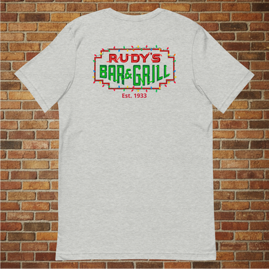 Back of Rudy’s Bar & Grill Christmas Neon Sign T-Shirt – festive neon NYC dive bar logo, flat lay, holiday shirt on brick wall background