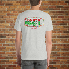 Load image into Gallery viewer, Back of Rudy’s Bar &amp; Grill Christmas Neon Sign T-Shirt on male model – festive NYC dive bar logo, holiday lights, brick wall background