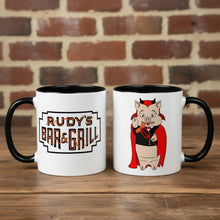 Load image into Gallery viewer, Rudy’s Bar &amp; Grill Halloween coffee mugs showing both sides—one with the classic Rudy’s logo, one with the devil pig cartoon—on a rustic wood bar with a brick wall background