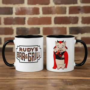 Rudy’s Bar & Grill Halloween coffee mugs showing both sides—one with the classic Rudy’s logo, one with the devil pig cartoon—on a rustic wood bar with a brick wall background