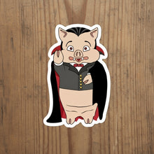 Load image into Gallery viewer, Rudy’s Bar &amp; Grill Dracula Pig Halloween sticker featuring a cartoon pig in a vampire costume, centered on a rustic wood background.