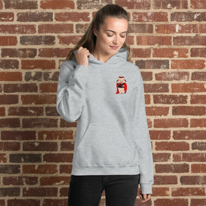 Woman wearing a sport grey hoodie with a small Baron Von Swine devil pig mascot on the chest, standing in front of a reddish-brown brick wall.