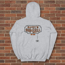 Load image into Gallery viewer, Sport grey hoodie laid flat with a large Rudy’s Bar &amp; Grill logo and hanging spider on the back, displayed against a reddish-brown brick wall background.