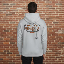 Load image into Gallery viewer, Man wearing a sport grey hoodie with a large Rudy’s Bar &amp; Grill logo and hanging spider on the back, standing in front of a reddish-brown brick wall.