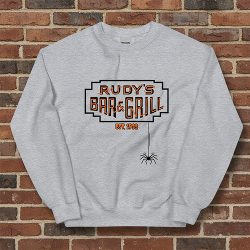 Sport grey crew neck sweatshirt with Rudy’s Bar & Grill Halloween logo and hanging spider, displayed flat against a reddish-brown brick wall background.