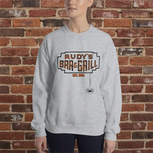 Load image into Gallery viewer, Woman wearing a sport grey crew neck sweatshirt with Rudy’s Bar &amp; Grill Halloween logo and hanging spider, standing in front of a reddish-brown brick wall.