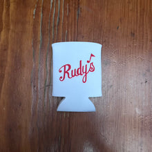 Load image into Gallery viewer, Flat lay of Rudy’s Bar &amp; Grill white can koozie with red script logo, displayed on a rustic wooden background