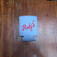 Load image into Gallery viewer, Flat lay of Rudy’s Bar &amp; Grill white can koozie with classic red script logo, on rustic wood table