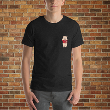 Load image into Gallery viewer, Front view of a black heather t-shirt with a small Baron Von Swine pig logo on the chest, modeled in front of a brick wall.