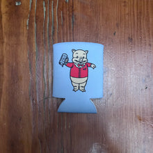 Load image into Gallery viewer, Flat lay of Rudy’s Bar &amp; Grill retro pig can koozie with Baron Von Swine mascot in red jacket, on rustic wooden surface