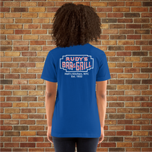 Load image into Gallery viewer, Back view of a woman wearing a true royal blue Rudy’s Bar &amp; Grill t-shirt with a neon sign logo and “Hell’s Kitchen, NYC Est. 1933,” standing in front of a brick wall.