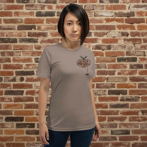 Female model wearing Rudy’s Bar & Grill Halloween edition t-shirt with bat and spider logo on pebble shirt, brick wall background.