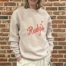 Load image into Gallery viewer, Close-up of Rudy’s Bar &amp; Grill vintage logo unisex relaxed crewneck sweatshirt in cream, brick wall background