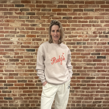 Load image into Gallery viewer, Full view of model wearing Rudy’s Bar &amp; Grill vintage logo unisex relaxed crewneck sweatshirt, standing in front of exposed brick wall