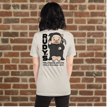 Load image into Gallery viewer, Woman wearing Rudy’s Bar &amp; Grill Halloween Edition heather dust t-shirt showing Baron Von Swine dressed as the Grim Reaper with vertical &quot;RUDY’S&quot; text and &quot;Halloween Edition Hell’s Kitchen - NYC&quot; on the back, standing against a brick wall background