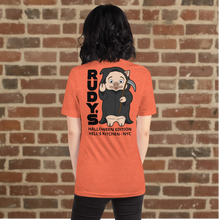 Load image into Gallery viewer, Woman wearing Rudy’s Bar &amp; Grill Halloween Edition heather orange t-shirt showing Baron Von Swine dressed as the Grim Reaper with vertical &quot;RUDY’S&quot; text and &quot;Halloween Edition Hell’s Kitchen - NYC&quot; on the back, standing against a brick wall background