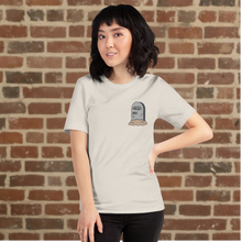 Load image into Gallery viewer, Woman wearing Rudy’s Bar &amp; Grill Halloween Edition heather dust t-shirt with a tombstone graphic on the left chest, standing against a brick wall background