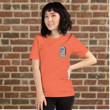 Load image into Gallery viewer, Woman wearing Rudy’s Bar &amp; Grill Halloween Edition heather orange t-shirt with a tombstone graphic on the left chest, standing against a brick wall background