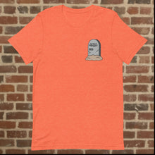 Load image into Gallery viewer, Front view of Rudy’s Bar &amp; Grill Halloween Edition orange t-shirt featuring a tombstone graphic with &quot;Rudy’s Bar &amp; Grill 1933-&quot; on the left chest, displayed on a brick wall background