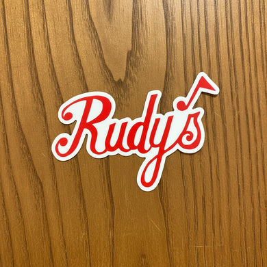 Red and white Rudy’s Jazz sticker with a musical note, displayed on a warm wood background