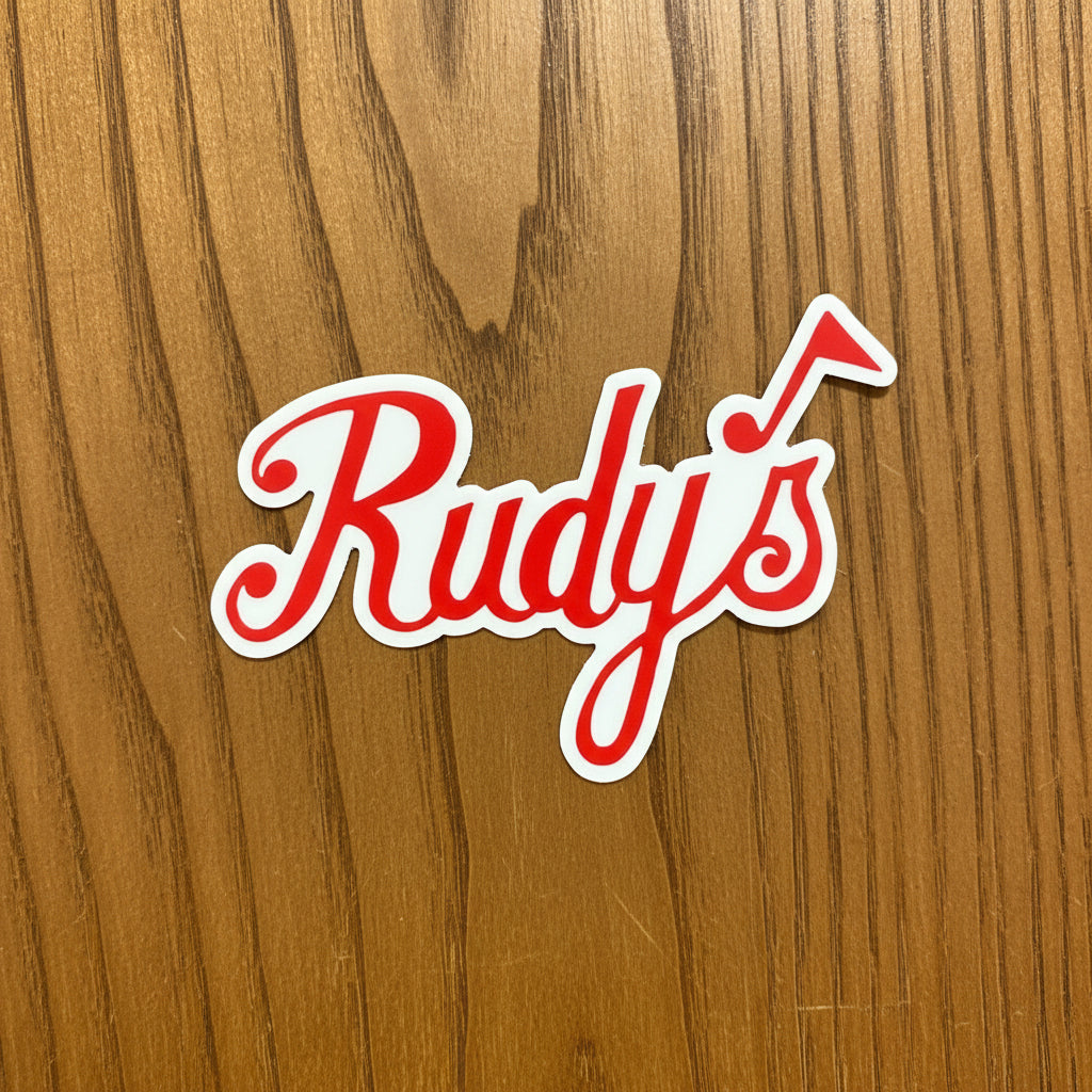 Red and white Rudy’s Jazz sticker with a musical note, displayed on a warm wood background