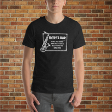 Load image into Gallery viewer, Male model wearing Rudy’s Bar &amp; Grill Jazz Saxophone T-Shirt in front of a brick wall