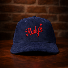 Load image into Gallery viewer, Rudy’s navy corduroy hat with red embroidered logo, displayed on wood surface with brick wall background