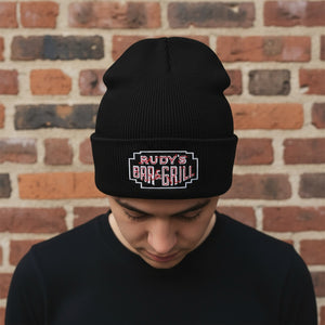 Male model wearing Rudy’s Bar & Grill Neon Sign Cuff Beanie, looking down in front of a brick wall