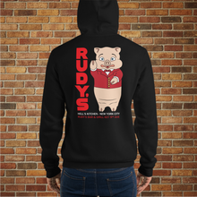 Load image into Gallery viewer, Back view of black hoodie featuring Rudy’s Bar &amp; Grill pig mascot and Hell’s Kitchen NYC address, shown on tattooed model in front of brick wall