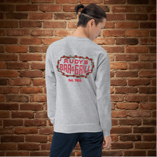 Load image into Gallery viewer, Person showing the back of a sport grey crew neck sweatshirt with Rudy’s Bar &amp; Grill neon sign design and “Est. 1933,” standing in front of a brick wall