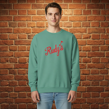 Load image into Gallery viewer, Man wearing seafoam Rudy’s St. Patrick’s Day sweatshirt with red Rudy’s logo, brick wall background.