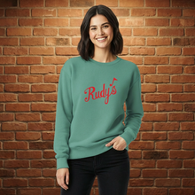 Load image into Gallery viewer, Woman wearing seafoam Rudy’s St. Patrick’s Day sweatshirt with red Rudy’s logo, brick wall background