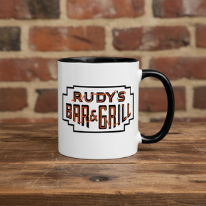 Rudy’s Bar & Grill Halloween coffee mug featuring the classic Rudy’s logo, placed on a rustic wood bar with a brick wall background