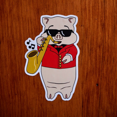 Baron Von Swine jazz pig sticker from Rudy’s Bar & Grill on wood background, wearing sunglasses and a red jacket while playing saxophone