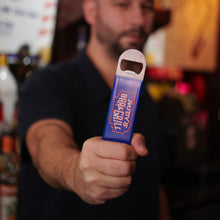 Load image into Gallery viewer, Bartender holding Rudy’s Bar &amp; Grill neon sign bottle opener at the bar