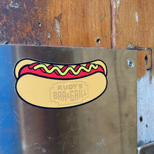 Load image into Gallery viewer, Rudy’s Bar &amp; Grill hot dog sticker displayed on metal surface at iconic NYC bar