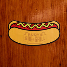 Load image into Gallery viewer, Rudy’s Bar &amp; Grill hot dog sticker on rustic wood background – NYC dive bar merchandise